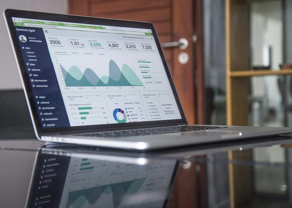 A laptop displaying various statistical graphs and charts sits on a reflective surface. The screen shows wavy line graphs, bar charts, and a pie chart with numerical data, suggesting a focus on maximizing off-season bookings through data analytics or business metrics.