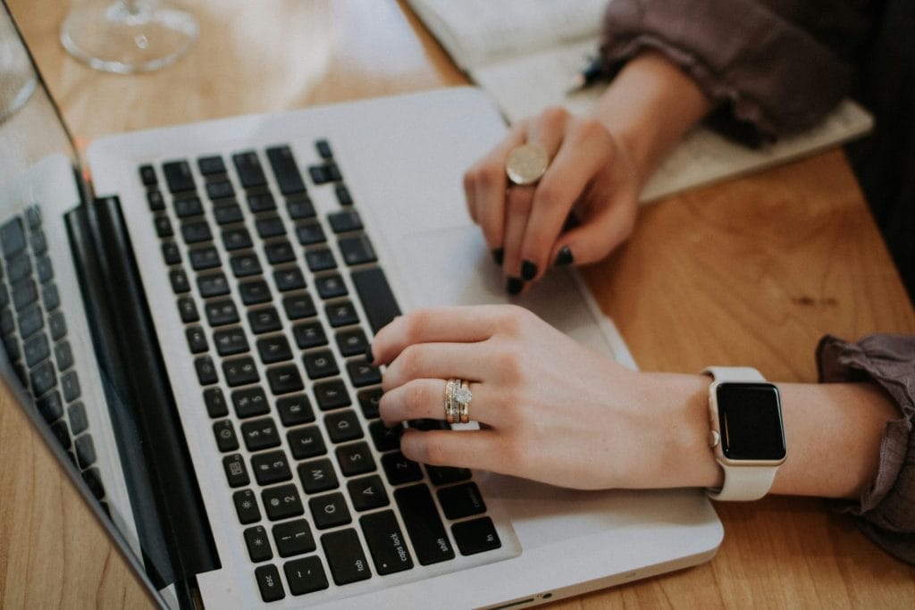 A woman is sitting in front of a Macbook and types.