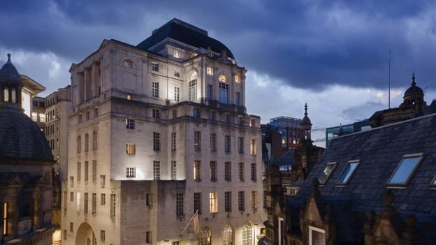 A historic stone building illuminated at dusk, beneath a dark, cloudy sky, offers classic architectural details and large windows. This captivating structure enhances the cityscape atmosphere while highlighting the property’s revenue potential in a prime location.